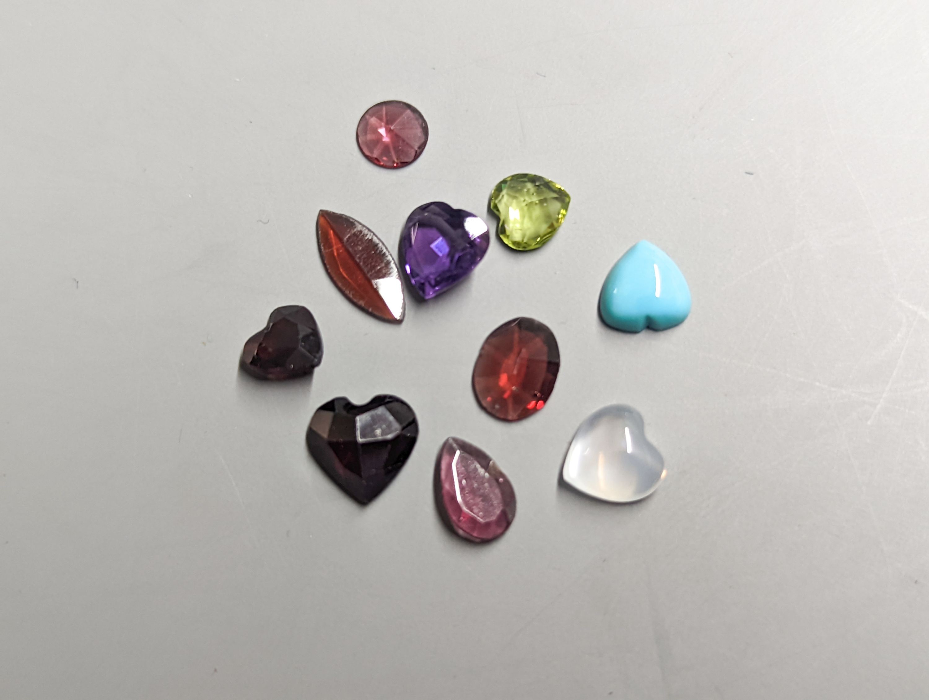 Nine assorted unmounted cut semi-precious gemstones including amethyst and garnet.